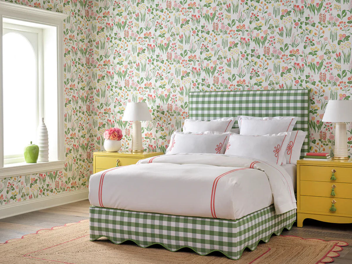 A brightly colored children's bedroom featuring patterned wallpaper, yellow side tables, and a green gingham bed frame.